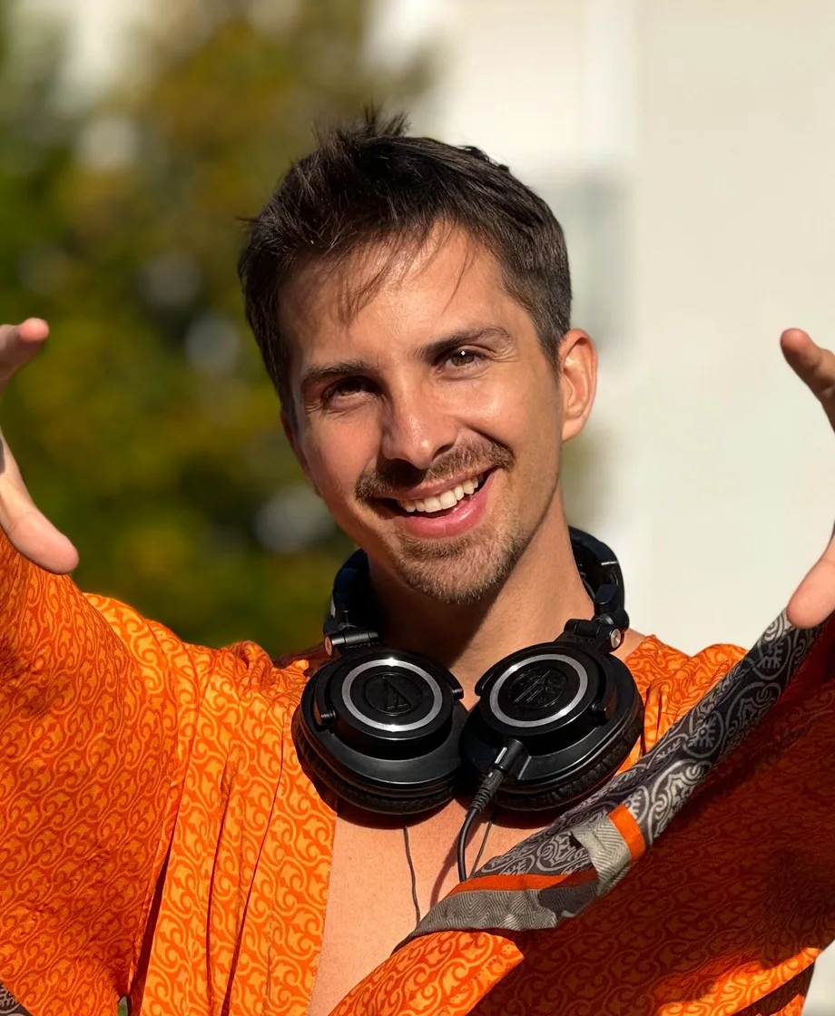 Mike Mana outdoors with headphones around his neck, arms open